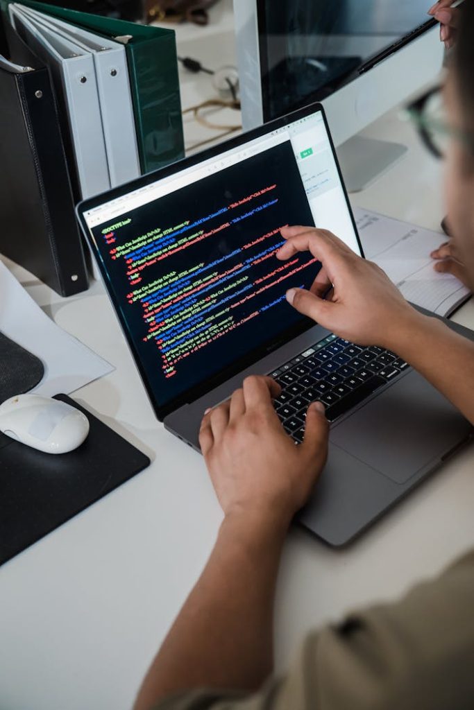 pexels-photo-12899188 Close-up of a programmer pointing at a colorful code script on a laptop in an office setting.